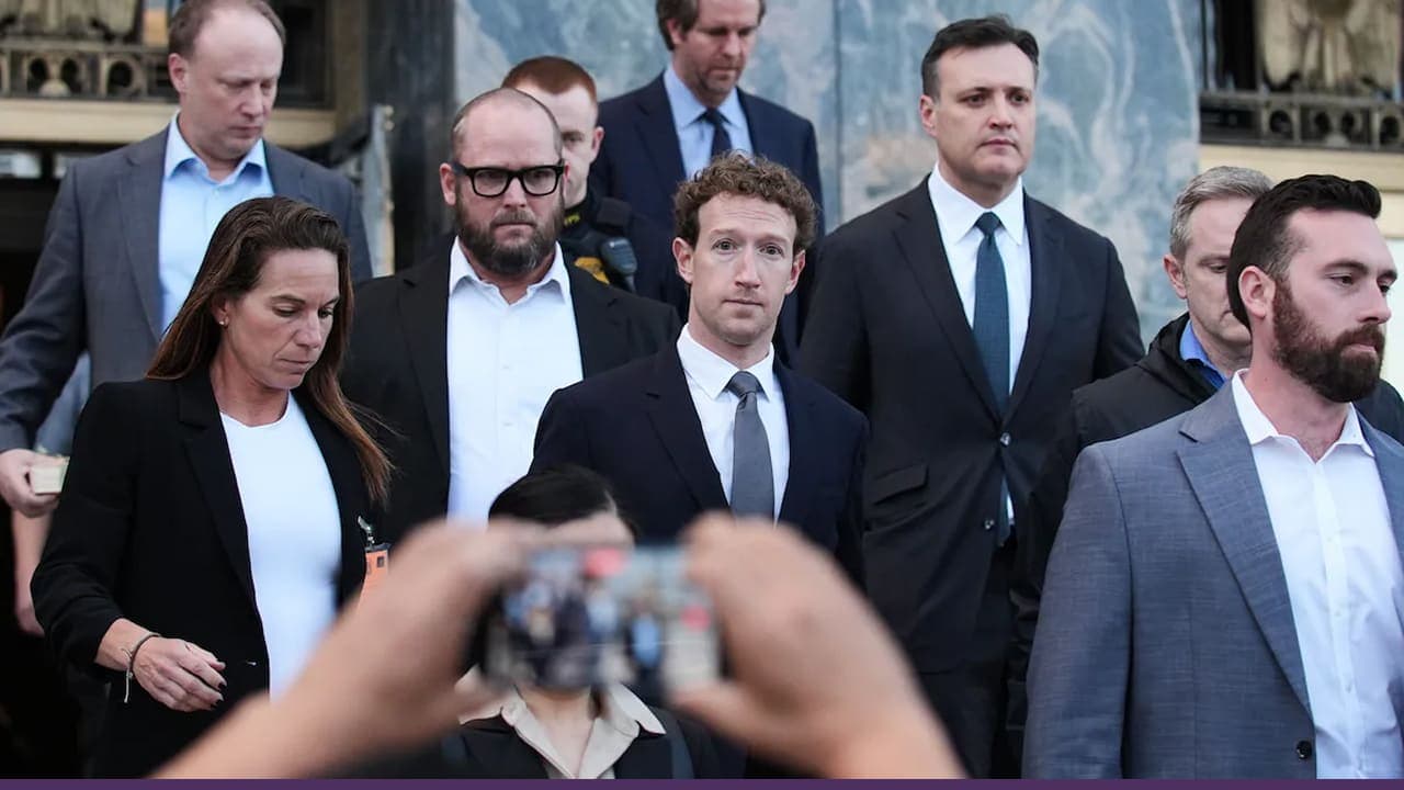A group of formally dressed individuals, including a man in a suit at the center, walk down steps outside a building while being photographed by someone holding a smartphone in the foreground.