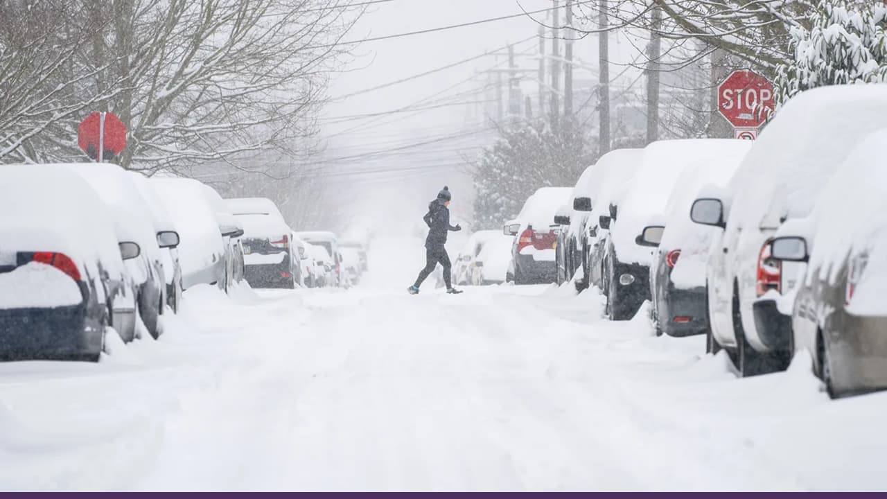 Pedestrian crossing snow-covered residential street during heavy winter storm