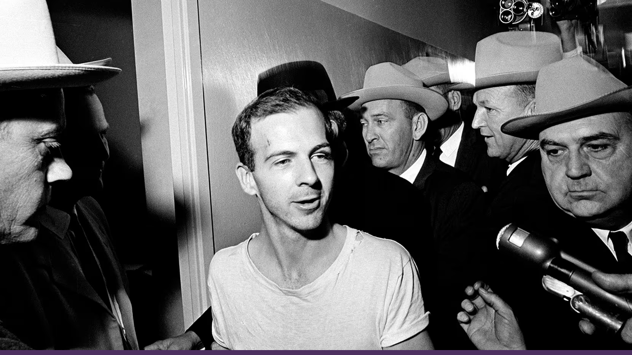 Lee Harvey Oswald, the accused assassin of President John F. Kennedy, is escorted by Dallas police through the corridor shortly before being fatally shot by Jack Ruby.
